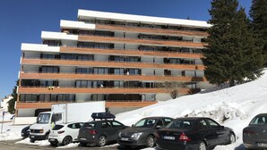 A multi-story hotel with a modern design, featuring balconies and a parking area with several cars. - Charming cabin studio *** 4/5 pers COZY at 50 m from the slopes (CHAMROUSSE)