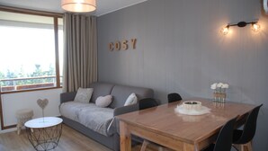 A modern living room with a grey sofa, a wooden dining table, and a small round table with a heart-shaped decoration. - Charming cabin studio *** 4/5 pers COZY at 50 m from the slopes (CHAMROUSSE)