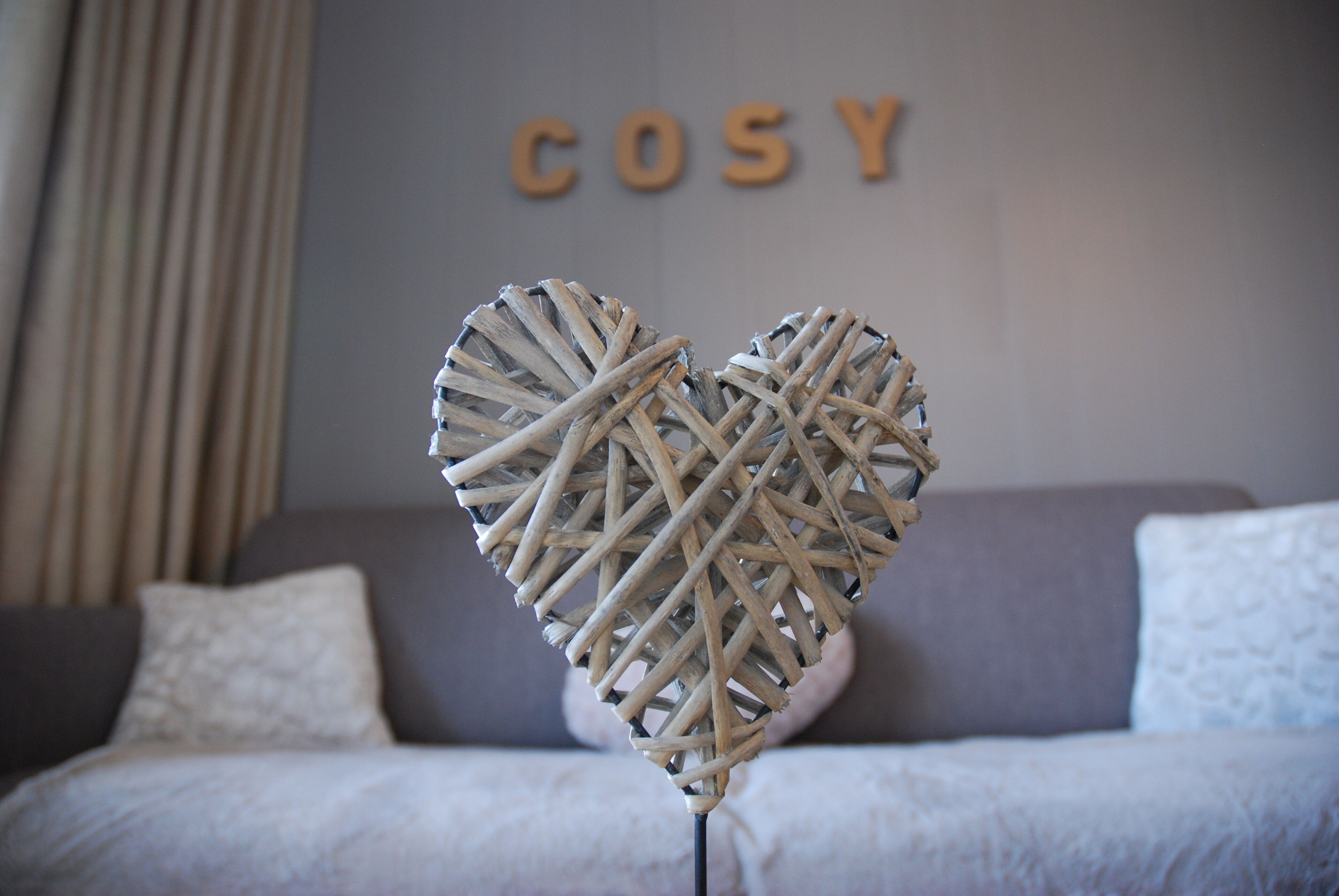 Et værelse med en grå sofa, en hjerteformet dekoration i hvid og ordet "COSY" på væggen.