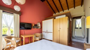Une chambre à coucher comprenant un lit, une télévision, une armoire en bois, un bureau avec des chaises et une fenêtre avec des rideaux.