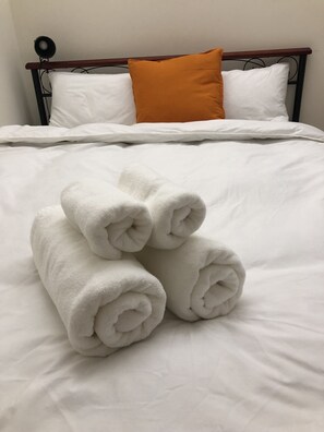 A neatly made bed with white linens and rolled towels in the center. - DayDay House (Taipei)