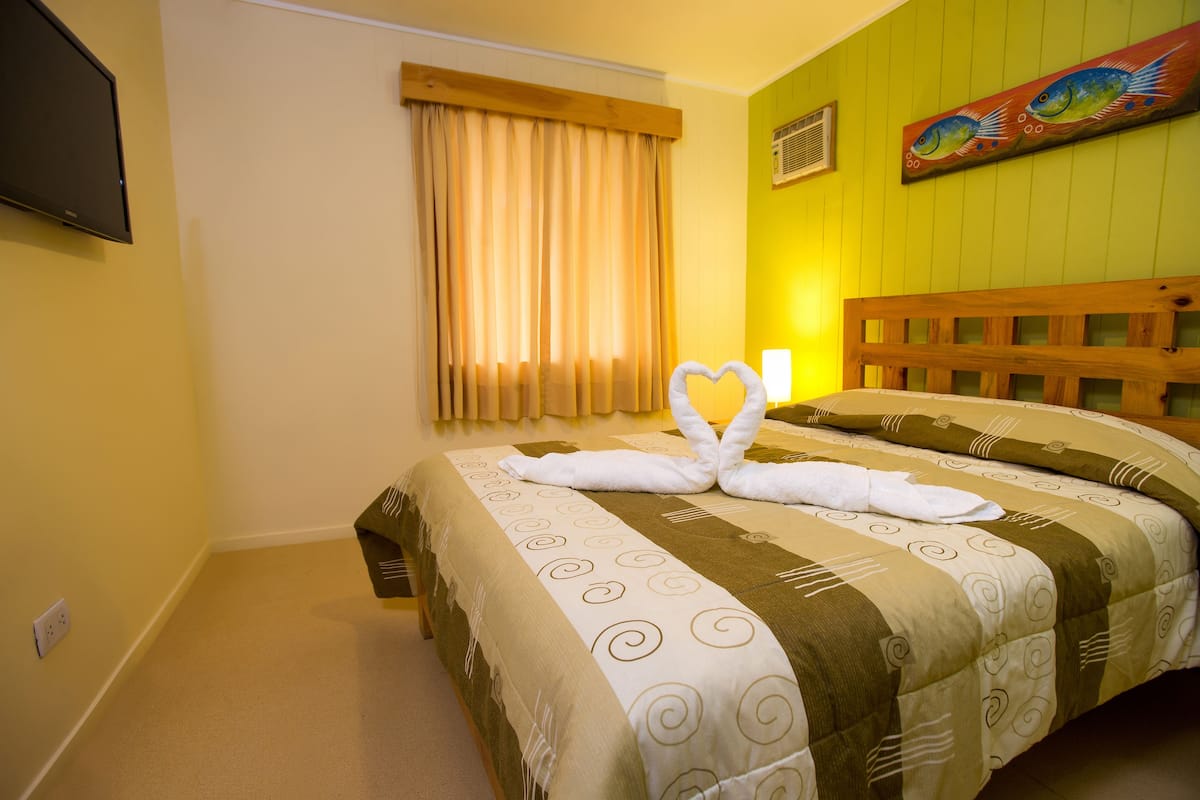 Une chambre d’hôtel avec un lit, un téléviseur fixé au mur et une fenêtre avec des rideaux.