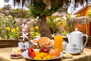 Un desayuno con diversas frutas, bollería y una cafetera sobre una mesa al aire libre.