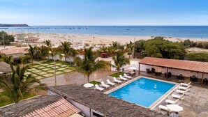 Zona de piscina con sillones de descanso, una piscina pequeña y vista a la playa y al océano.