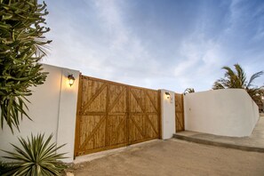 Una verja de madera con un muro blanco y un camino de hormigón que conduce a un edificio.