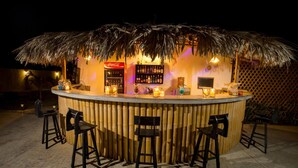 Un bar tiki con techo de paja, taburetes de bar y un refrigerador de Coca-Cola.