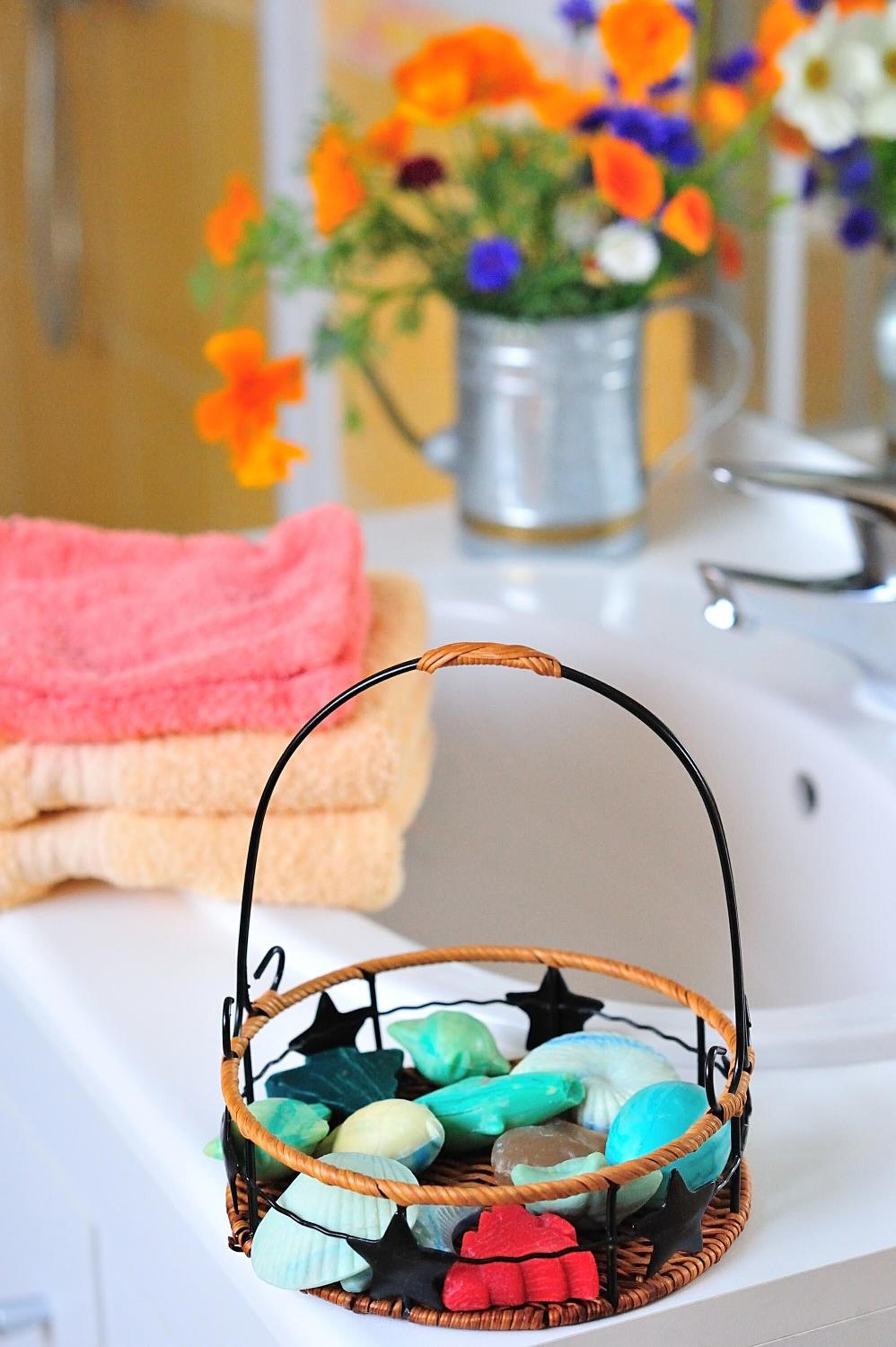 A bathroom with a basket of colorful bath items, a pink towel, and a vase of flowers.