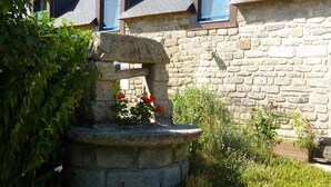 A stone structure with a flower arrangement in a garden area, surrounded by lush greenery and white flowers. - Ti Er Mad (Kernascleden)