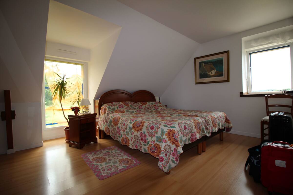 A bedroom with a bed, a nightstand, a lamp, a chair, a window, and a painting on the wall.