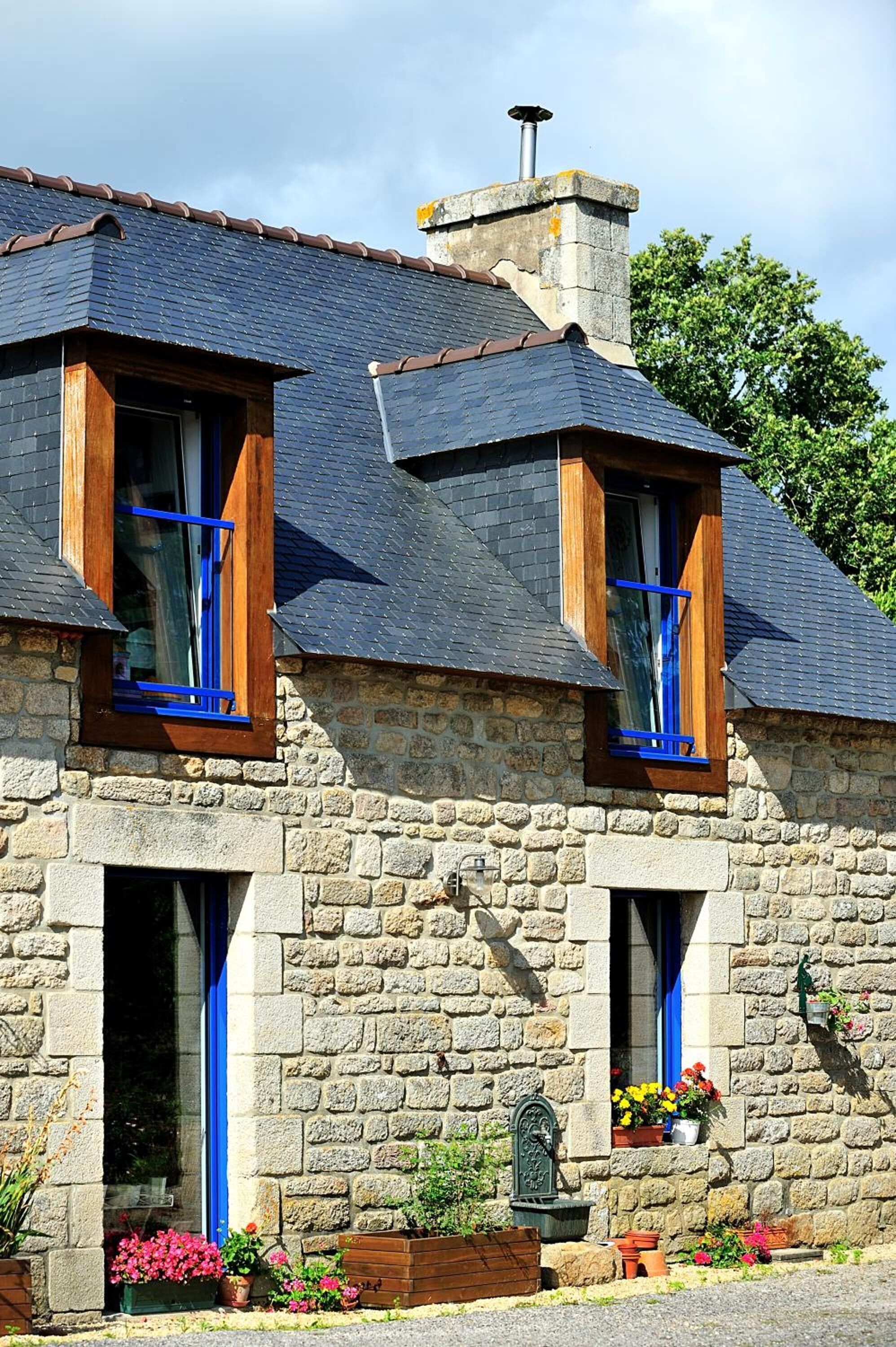 A stone house with two windows, a chimney, and a flower box.