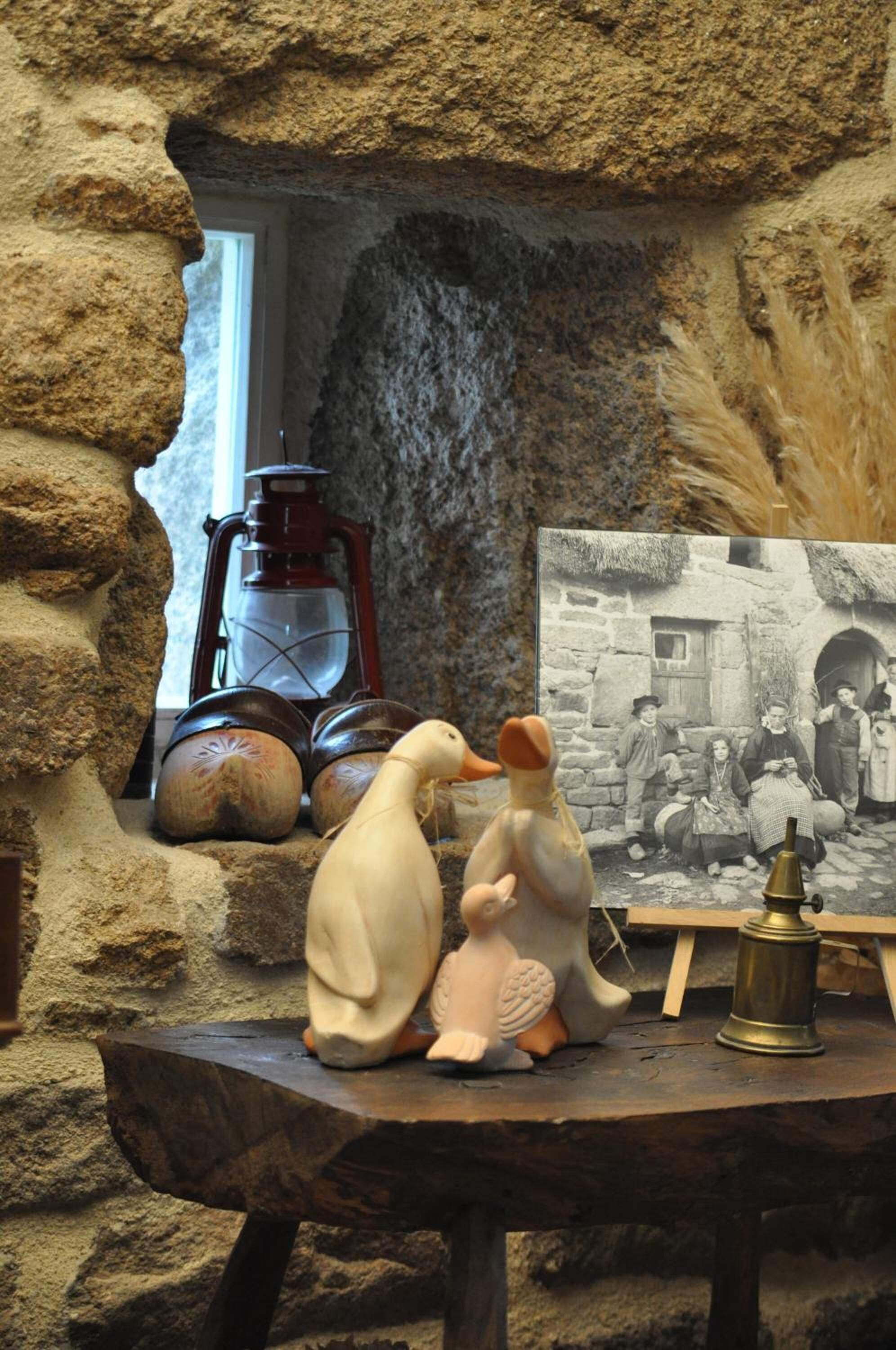 A rustic stone wall with a small table holding a lantern, a vintage photograph, and decorative items.