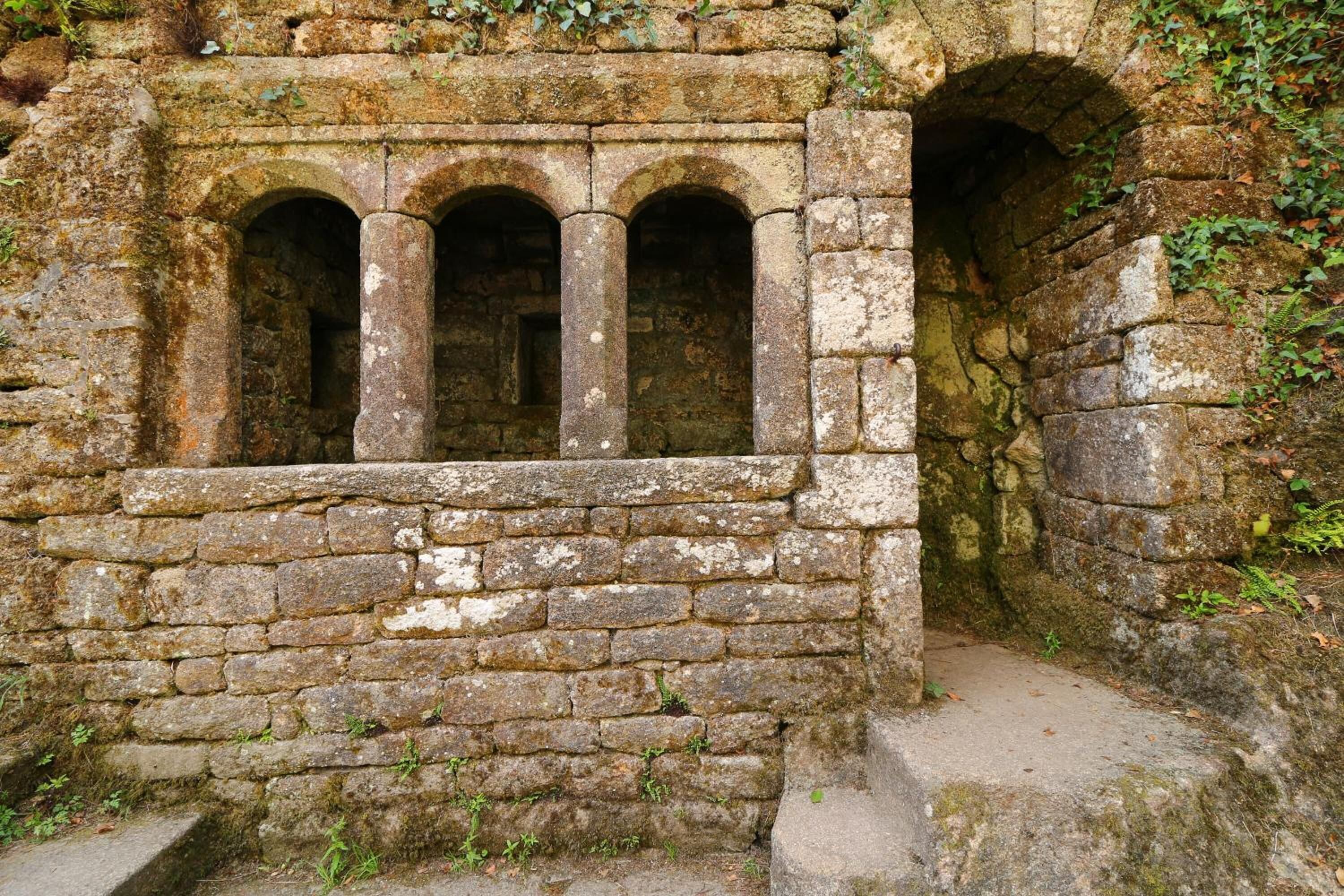 An ancient stone structure with three arched windows and a stone staircase leading up.