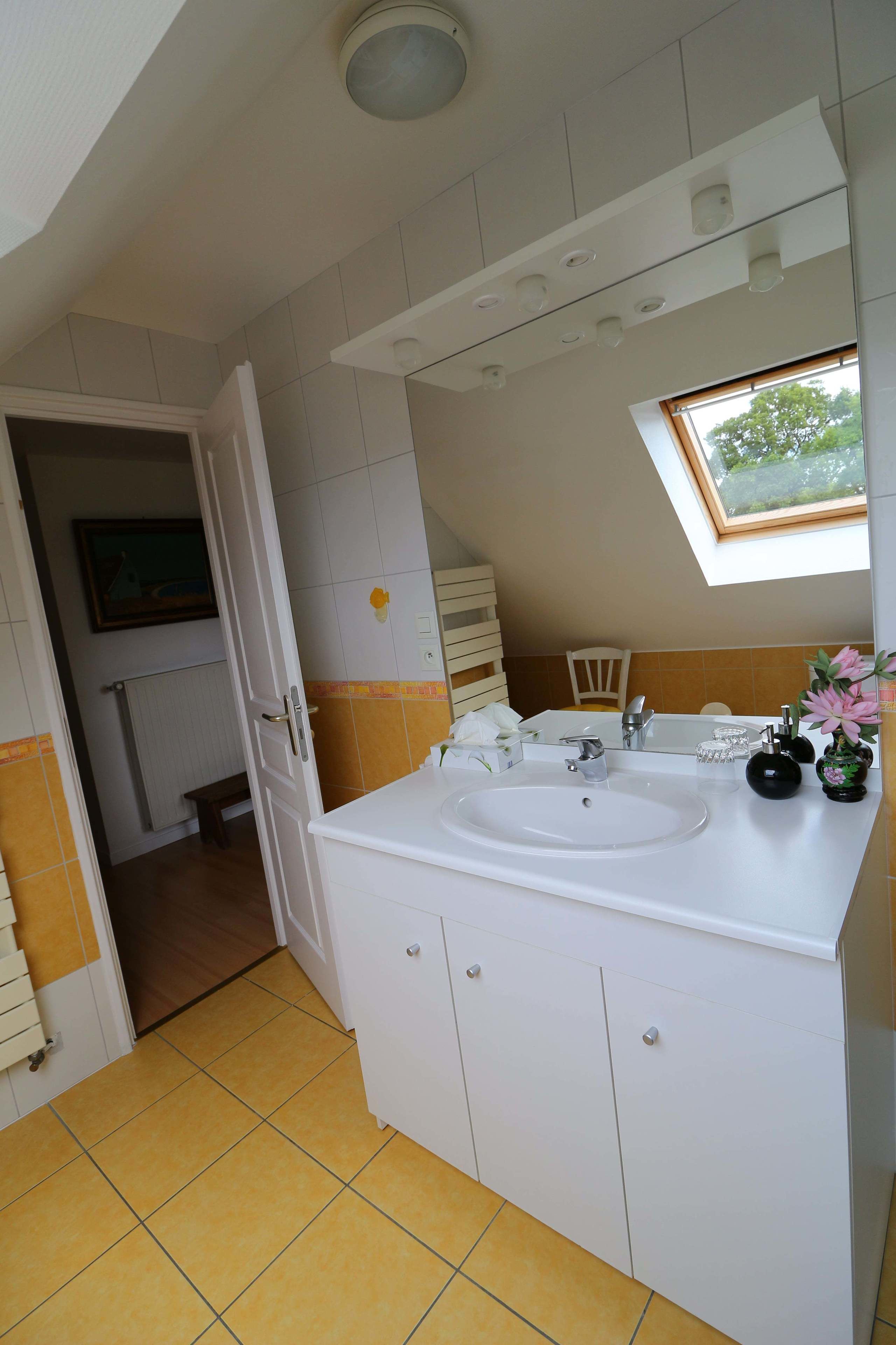 Un baño con lavamanos blanco, un espejo y una ventana sobre el lavamanos.
