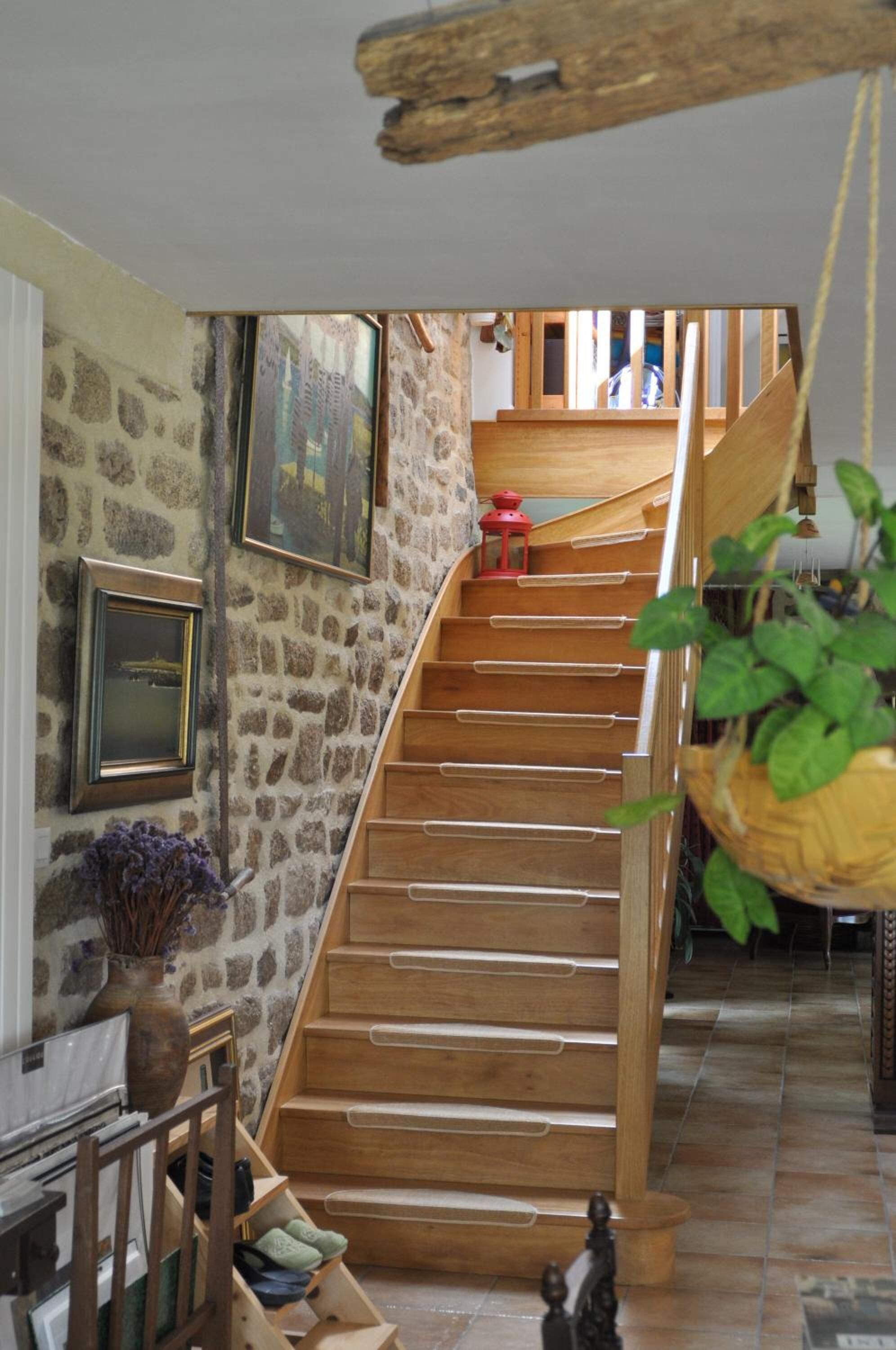 A wooden staircase with a stone wall on one side, a hanging plant, and a red lantern.