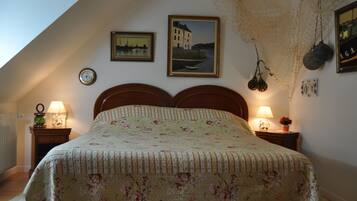 A bedroom with a bed, two bedside tables, a wall clock, two framed pictures, and a hanging net.