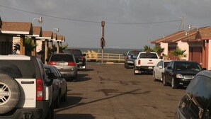 A parking lot with several cars parked in rows, a wooden fence, and buildings with a uniform architectural style. - Bayfront Cottages (Rockport)