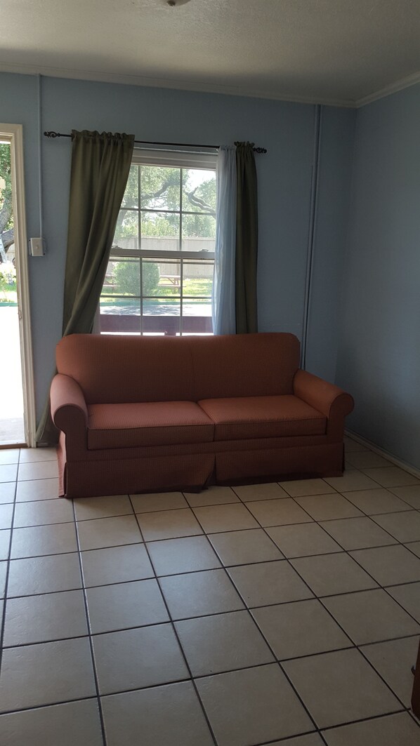 Quarto com sofá, janela com cortinas e piso em azulejos.