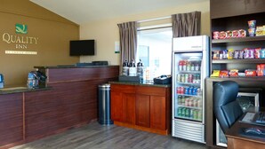 A hotel reception area with a wooden counter, a television, a refrigerator stocked with beverages, and a seating area with a laptop and chair. - Rodeway Inn & Suites Ontario (Ontario)