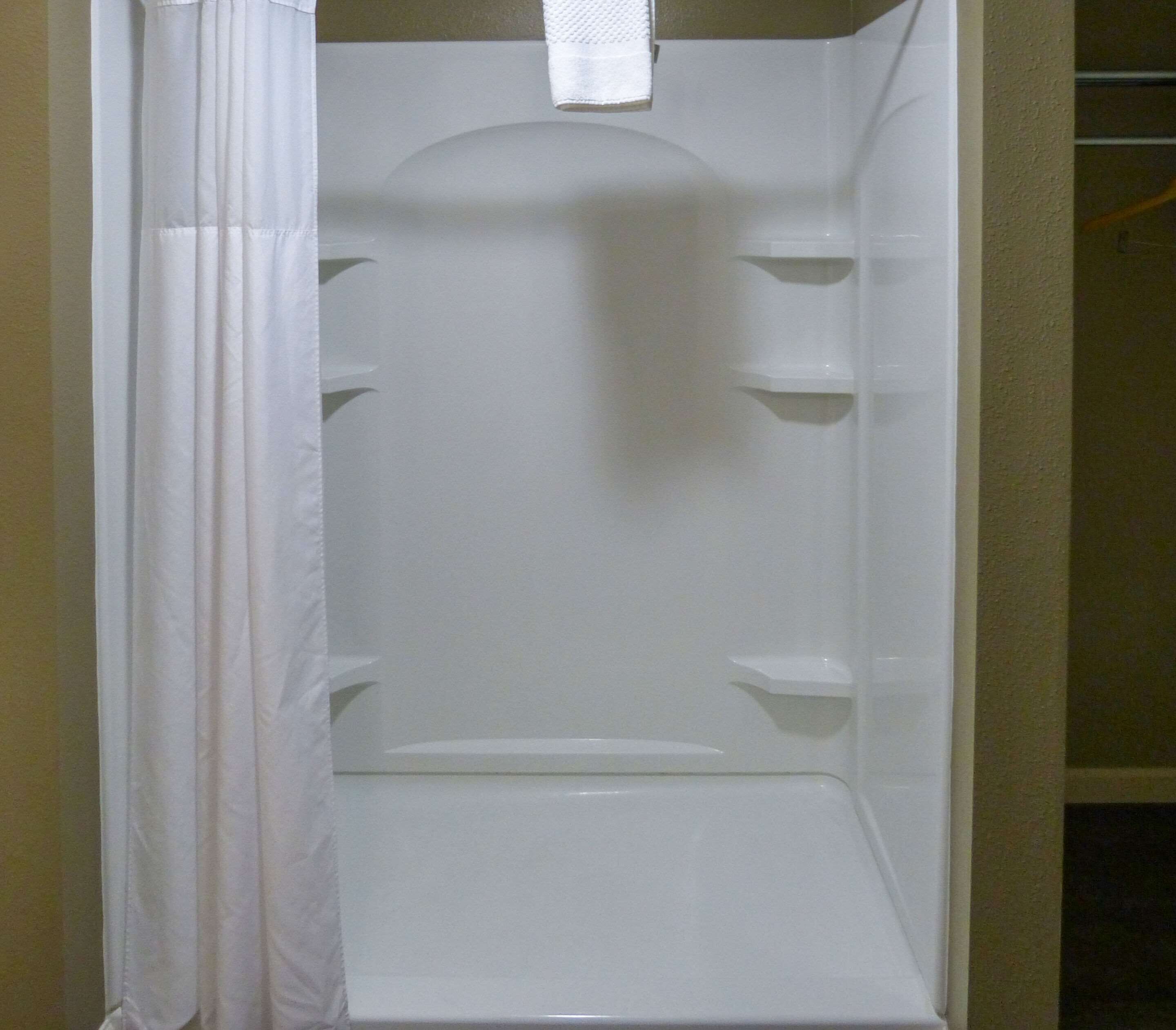 Un box de ducha blanco con cortina, un perchero y una repisa.
