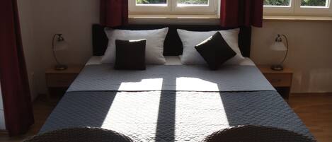 Una cama con colcha acolchada, dos mesitas de noche con lámparas y una ventana con cortinas.