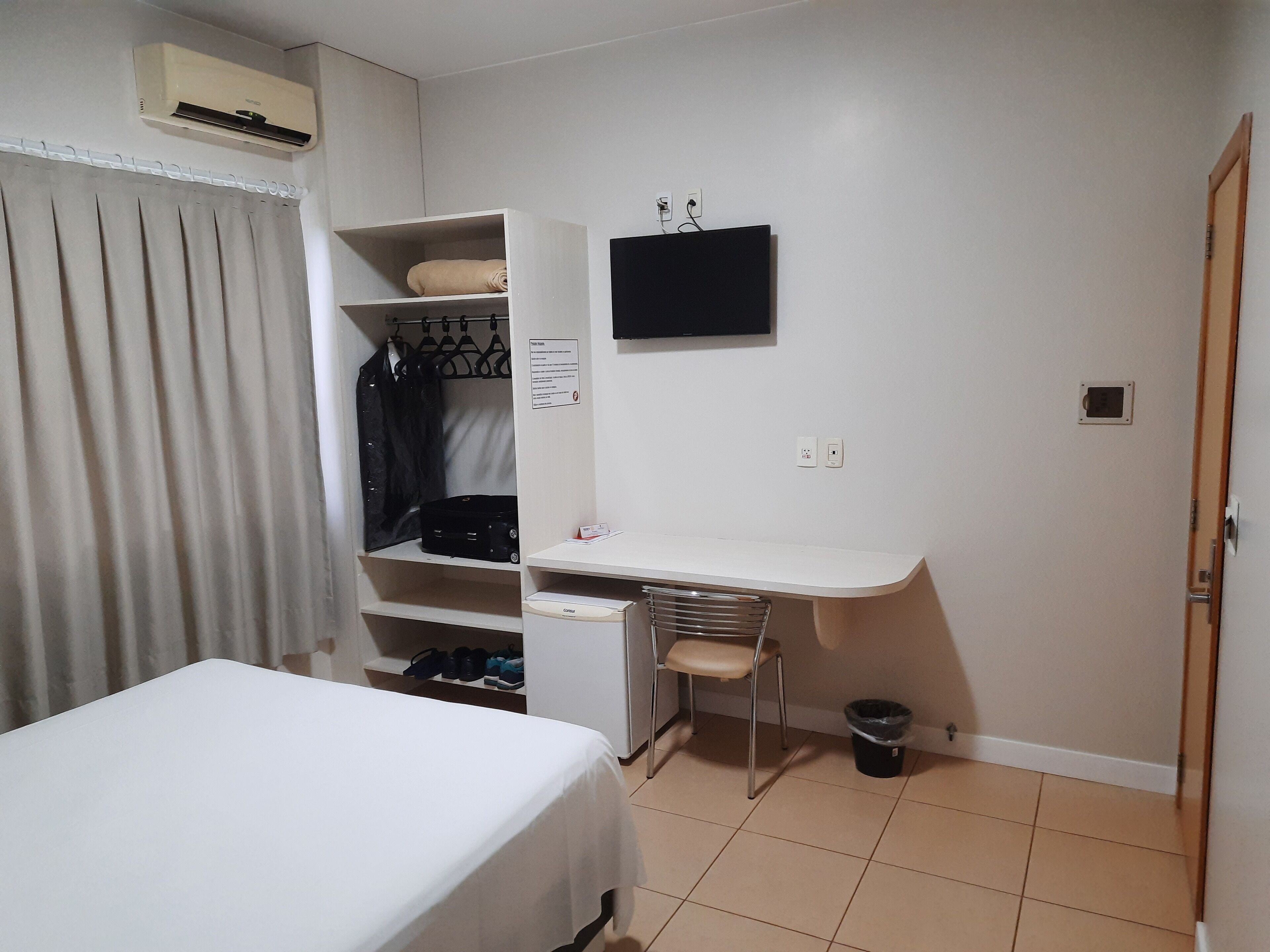 A small, neatly organized bedroom with a bed, a desk, a chair, and a wardrobe.