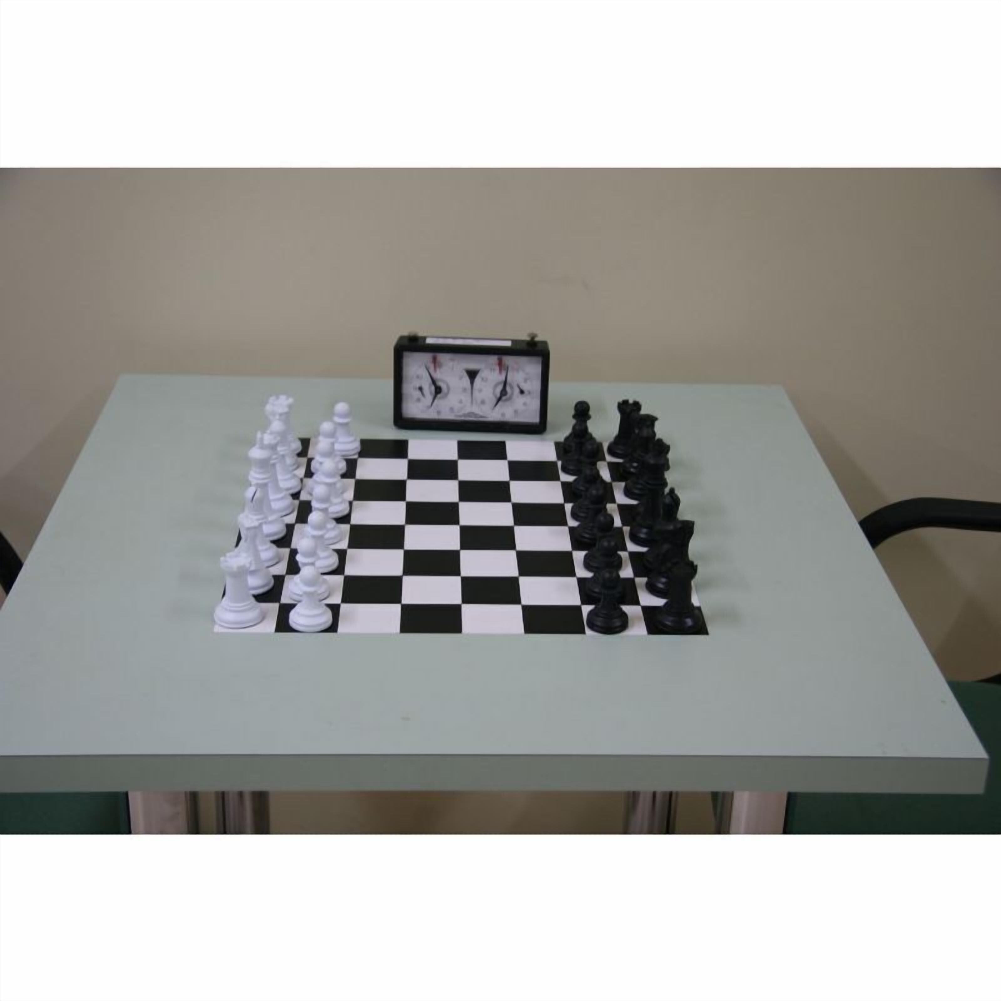 Un tablero de ajedrez con las piezas dispuestas para jugar, un reloj y una mesa frente a una pared lisa.