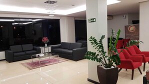 Un vestíbulo moderno con sofás negros, una mesa de centro, una planta roja y un letrero que indica la salida.
