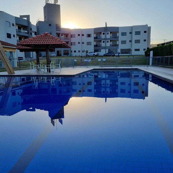 Una piscina con reflejo cristalino, rodeada de edificios modernos y un pequeño pabellón.