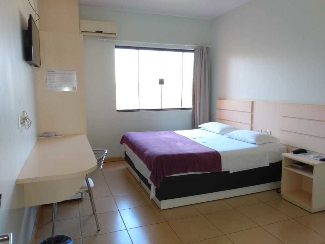 A hotel room with a bed, a desk, a chair, a TV, and a window with curtains.