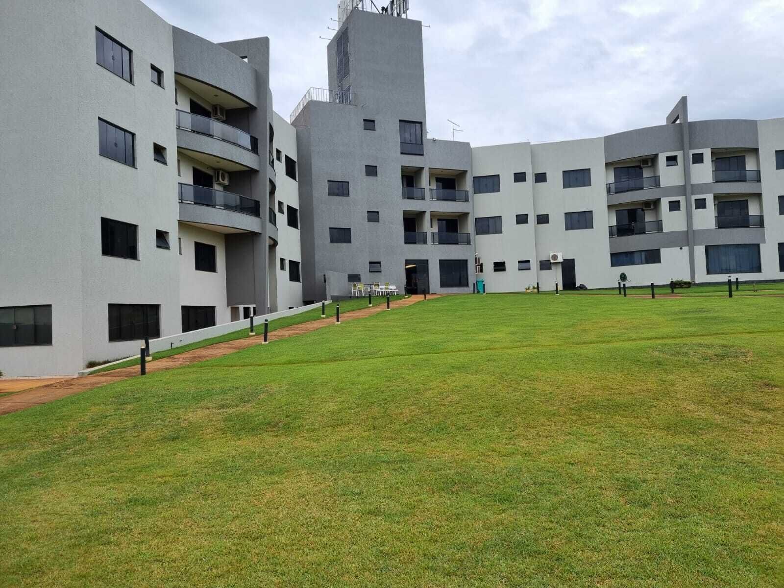 A modern multi-story residential building with balconies, a grassy courtyard, and a clear sky.