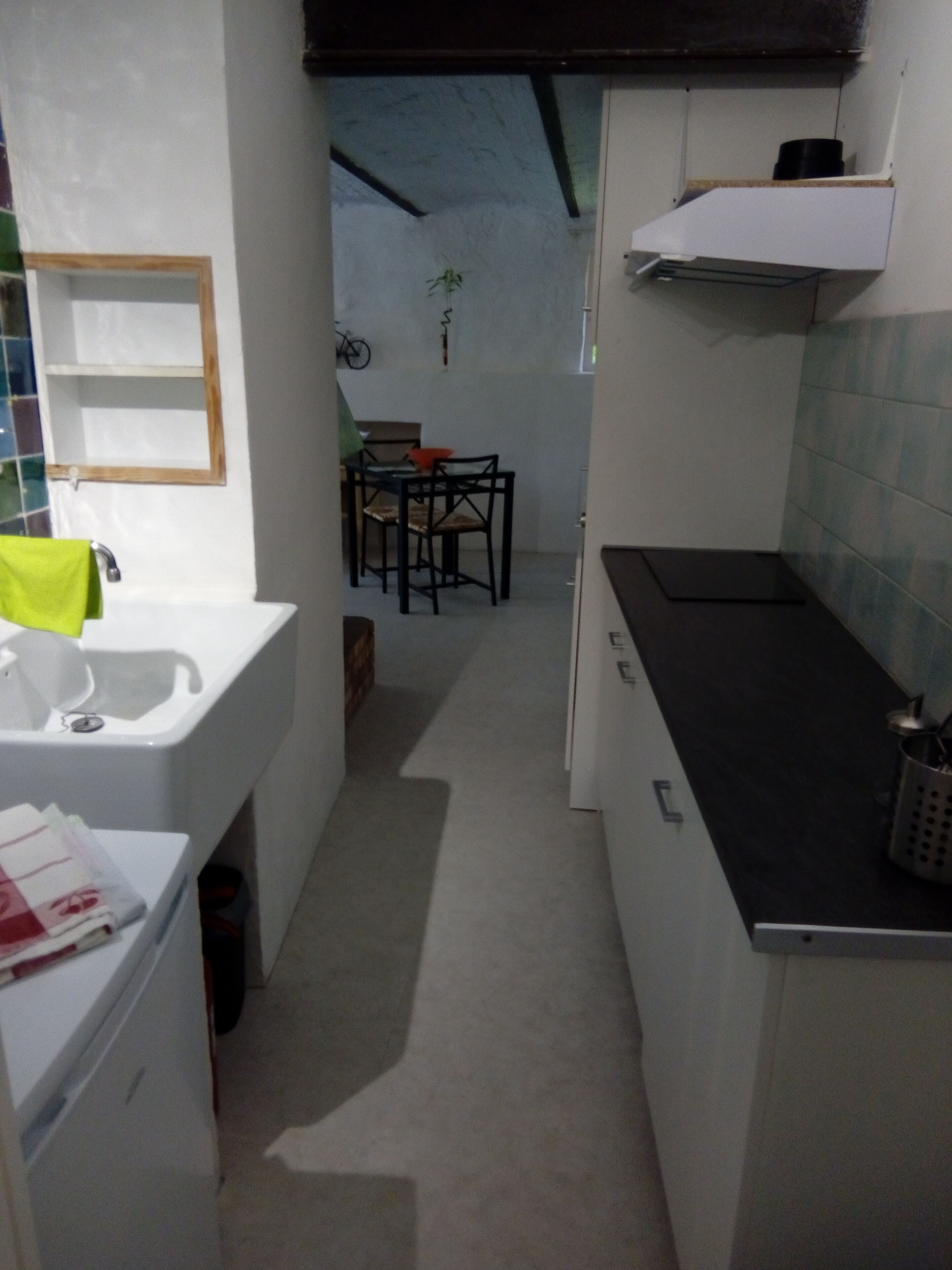 A narrow kitchen with white cabinets, a black countertop, and a dining area with chairs and a table.
