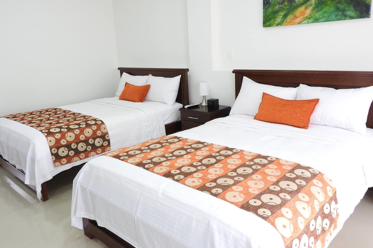 Two single beds with white linens and orange patterned bedspreads, a nightstand with a lamp, and a painting on the wall.