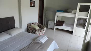 A bedroom with a bed, a floral armchair, a bunk bed, and a small cabinet.