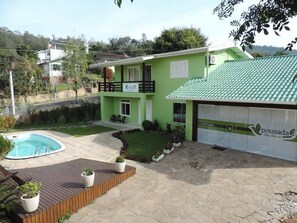 A green house with a swimming pool, a wooden deck, and a paved patio. - Pousada Três Coroas (Tres Coroas)