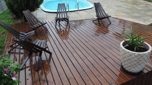 Een houten terras met een jacuzzi, omgeven door groen en een huis op de achtergrond.
