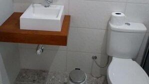 Een badkamer met een wit wastafel, een houten aanrechtblad, een spiegel, een toilet en een prullenbak.