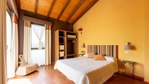 Ein Schlafzimmer mit Holzboden, einem Bett mit weißer Decke, einem hölzernen Schrank und einem kleinen Tisch mit Lampe.