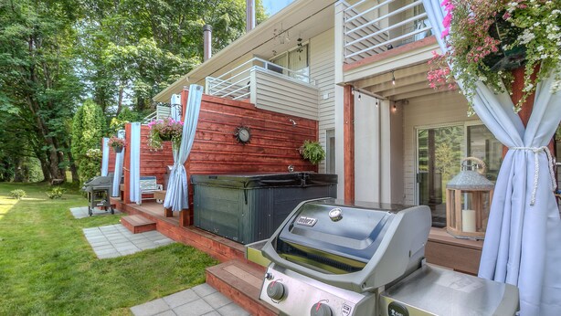 Patio trasero con una parrilla, una terraza de madera y una casa con balcón.
