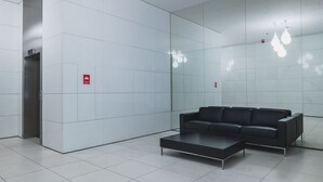 Un vestíbulo moderno con un sofá de cuero negro, una mesa de centro y una pared de vidrio que refleja luminarias.