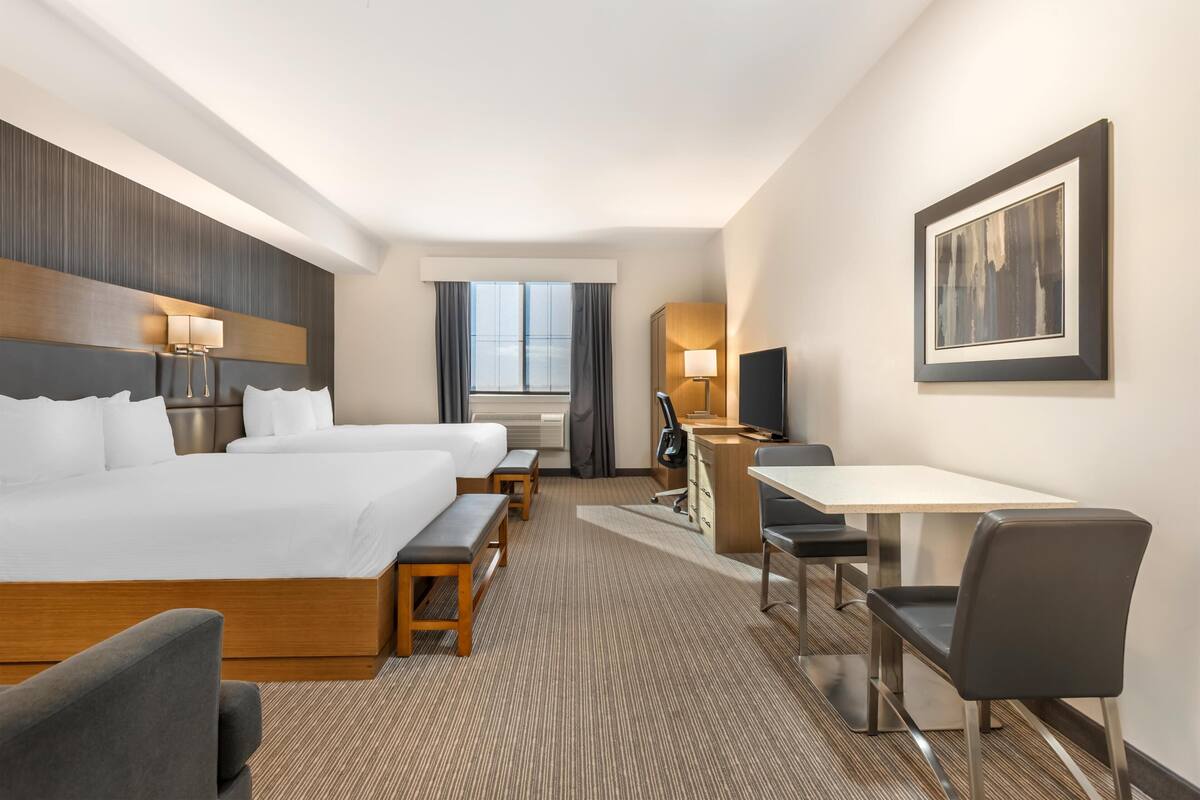 Una habitación de hotel con una cama grande, un escritorio, una silla, un televisor y un cuadro en la pared.