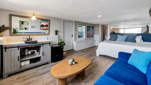 A modern bedroom with a bed, a blue sofa, a wooden table, and a bathroom with a sink and cabinets. - Oceanfront retreat w/ AC & beach access (Laguna Beach)