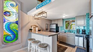 A kitchen with a central island, bar stools, a refrigerator, and a coffee maker. - Oceanfront retreat w/ AC & beach access (Laguna Beach)