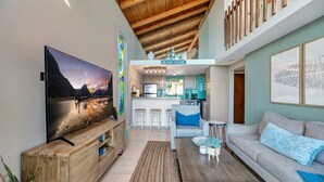 A modern living room with a large TV, wooden furniture, a sofa, and a kitchen area in the background. - Oceanfront retreat w/ AC & beach access (Laguna Beach)
