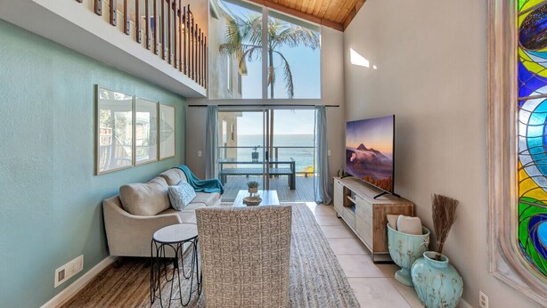 A spacious living room with a large TV, a sofa, a coffee table, and a view of the ocean through large windows. - Oceanfront retreat w/ AC & beach access (Laguna Beach)
