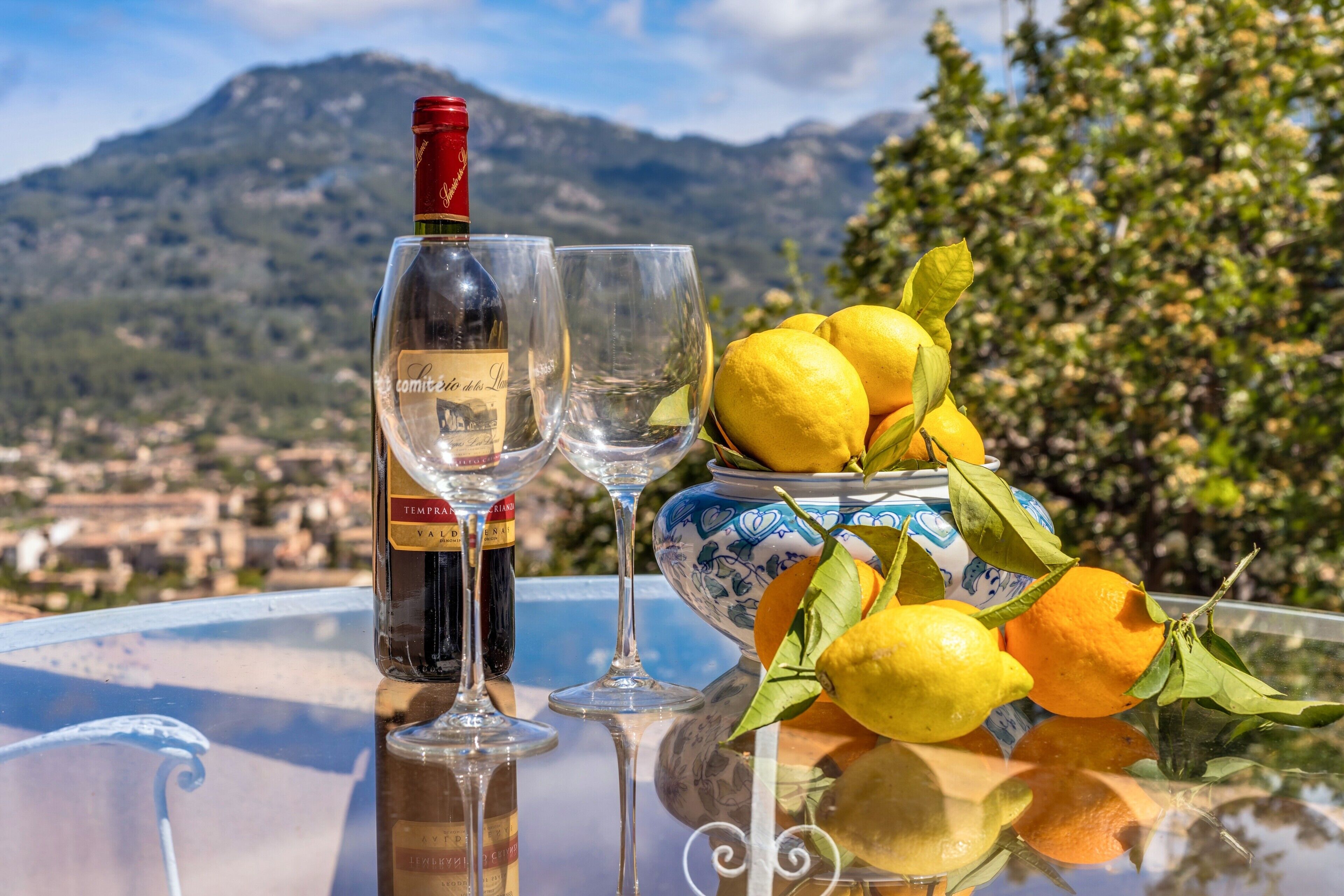 A table with a bottle of wine, two glasses, and a bowl of lemons.
