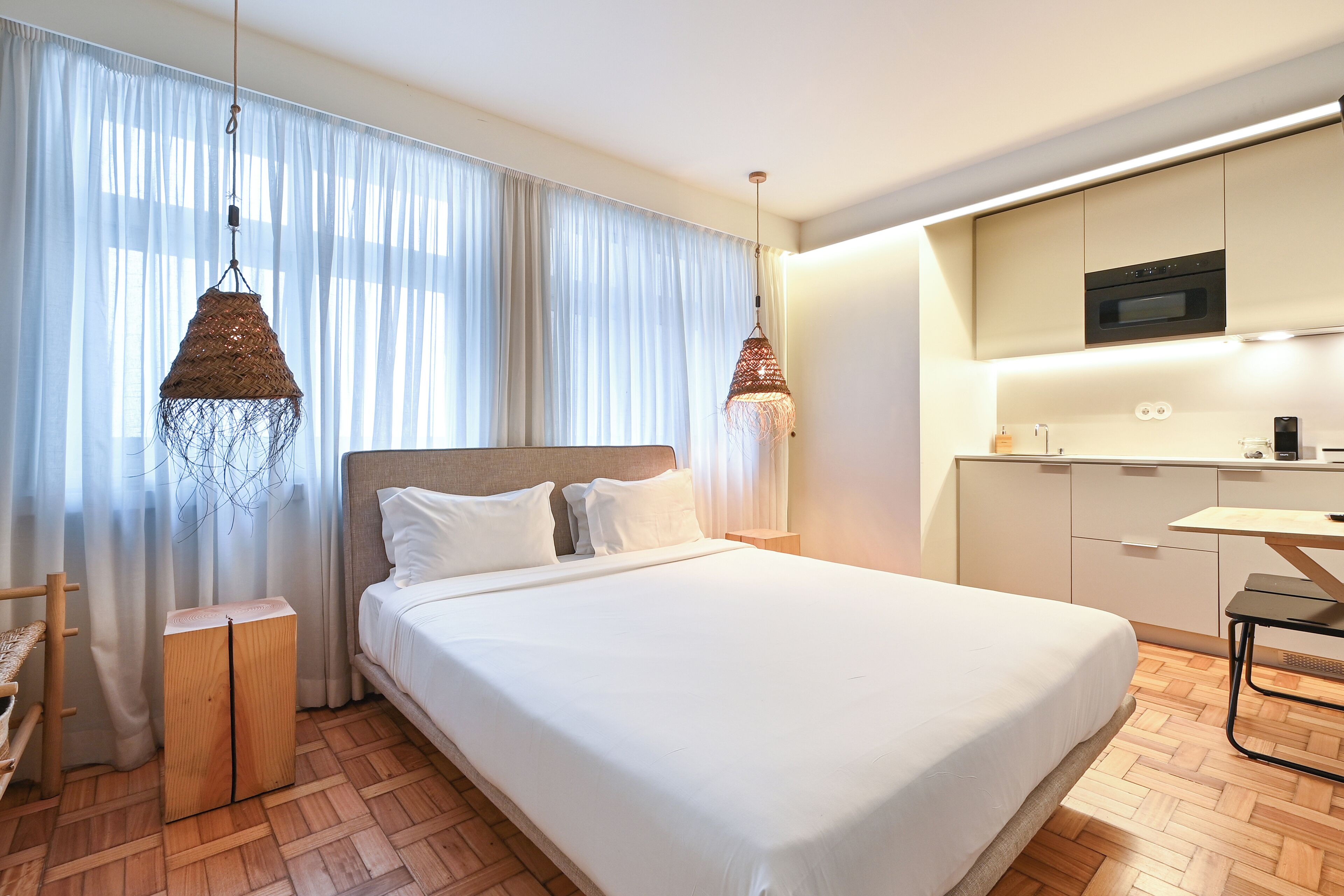 Une chambre d’hôtel moderne dotée d’un grand lit, d’un plancher en bois, d’une kitchenette et de deux luminaires suspendus.