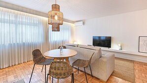 En moderne stue med et rundt bord, fletstole, en sofa, et fjernsyn og en loftslampe.