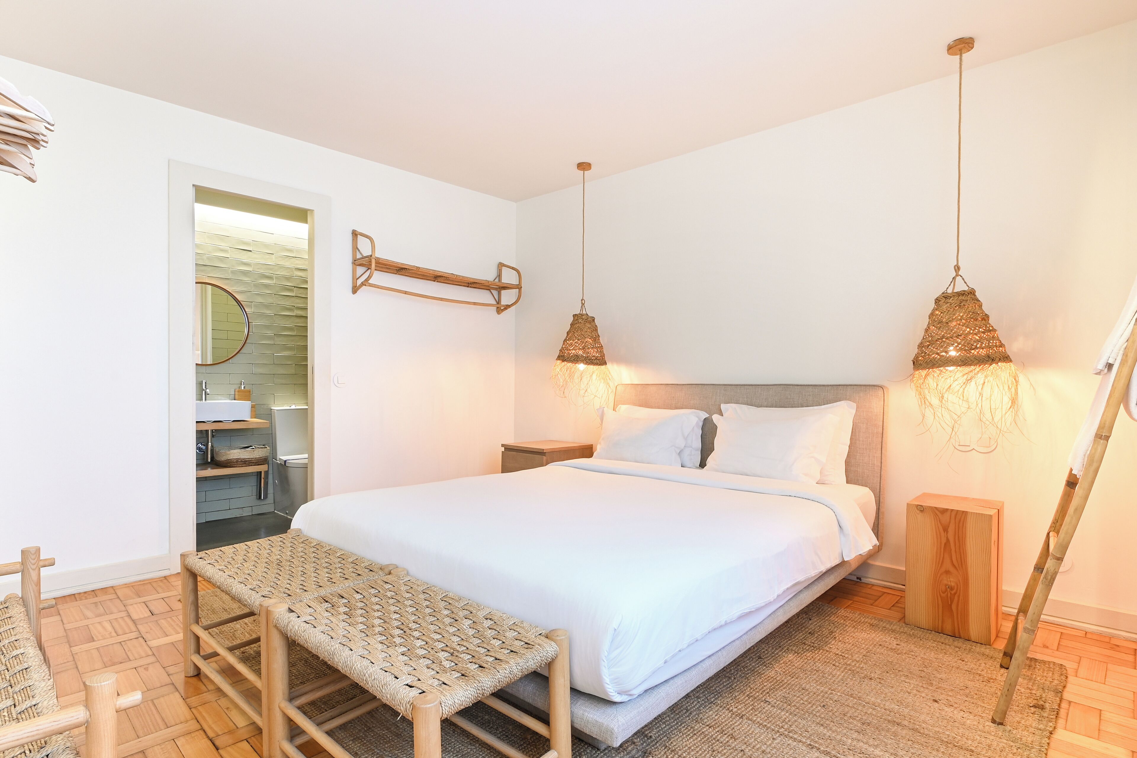 Een slaapkamer met een groot bed, twee nachtkastjes, een bankje, een houten trap en een hanglamp.