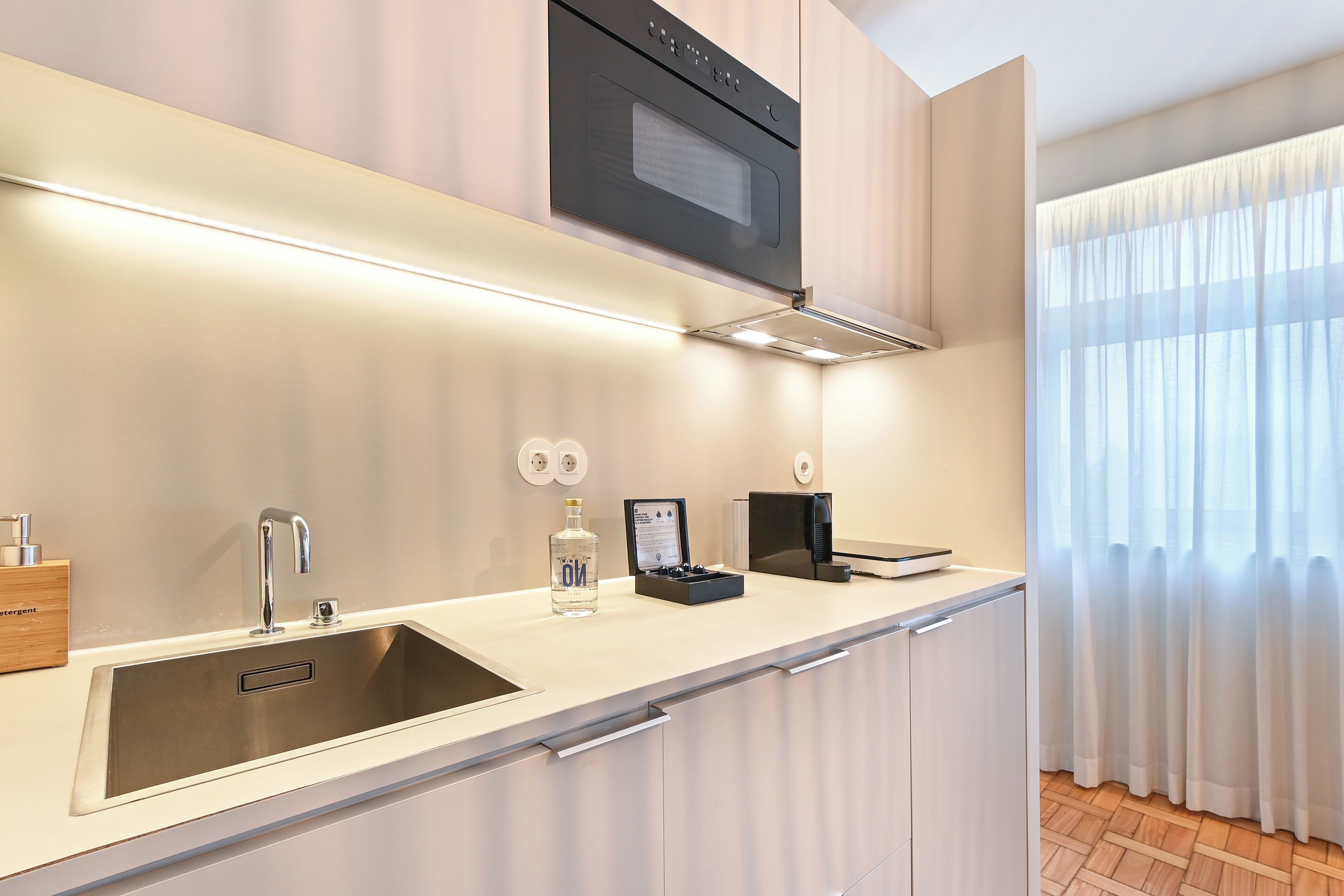 A modern kitchen with a stainless steel sink, a built-in oven, and a microwave above the counter.