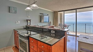 Een keuken met een groot eiland, een eethoek met uitzicht op de oceaan, en een balkon met een tafel en stoelen.